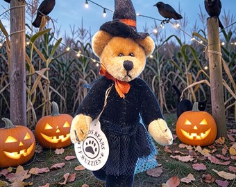 May include: A teddy bear dressed as a witch, wearing a black dress, hat, and orange scarf. The bear is holding a tag that says "OS BEARS TY WIZZIES". The background includes carved pumpkins, crows, and a cornfield, creating a Halloween theme.