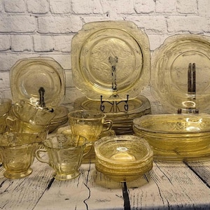 May include: A collection of vintage amber-colored glassware, including plates, bowls, and teacups, arranged on a wooden surface. The glassware features a delicate floral pattern, creating an elegant and classic aesthetic. The set includes various sizes and shapes.