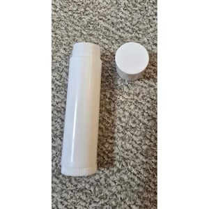 May include: A cylindrical white plastic lip balm tube with a matching removable white cap. The tube features a ridged base for twisting the product up and down. The container is plain, smooth, and opaque, designed for holding cosmetic or skincare balms.