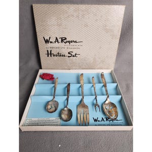 May include: A vintage Wm. A. Rogers Hostess Set in its original box. The set includes serving spoons, a fork, and a serving fork. The box is light beige with a polka dot pattern and the text "Wm. A. Rogers" and "Hostess Set".