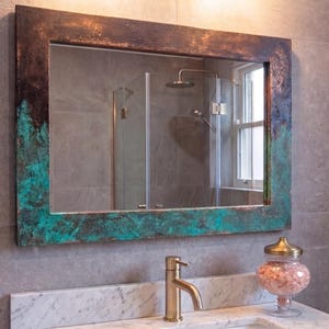 May include: A rectangular wall mirror featuring a wide, textured frame with a weathered finish. The frame displays a dark brown, oxidized metal appearance with prominent patches of vibrant turquoise verdigris patina across the surface.