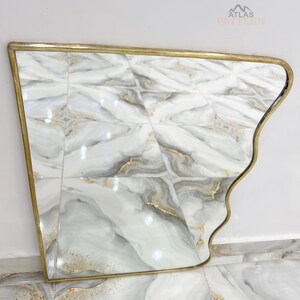 May include: A gold-framed mirror with a wavy, asymmetrical design. The mirror reflects a white and grey marble tiled floor.