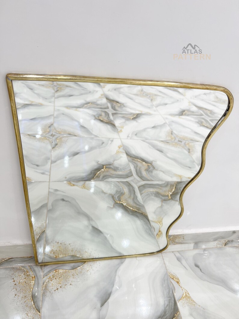 May include: A gold-framed mirror with a wavy, asymmetrical design. The mirror reflects a white and grey marble tiled floor.