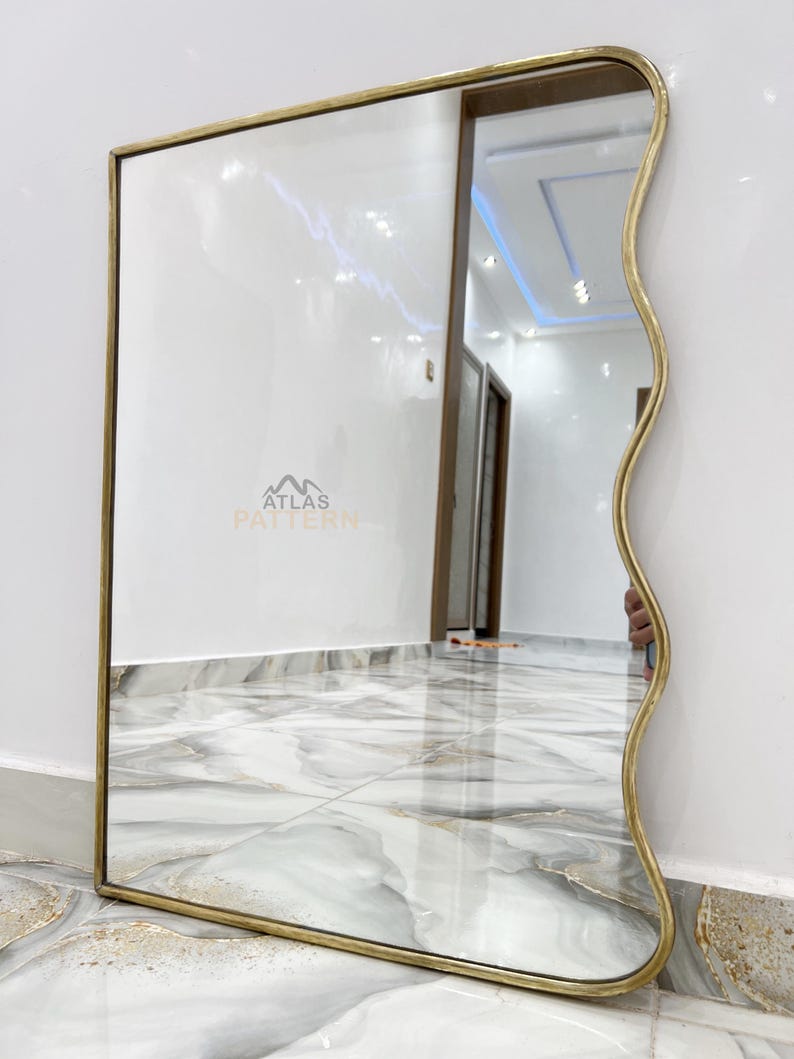 May include: A gold-framed mirror with a wavy edge. The mirror is reflecting a hallway with a tiled floor.