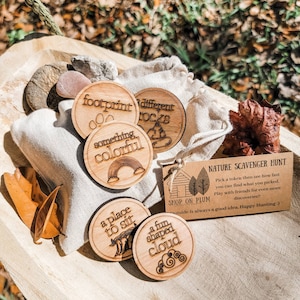May include: A set of wooden nature scavenger hunt tokens with phrases like "footprint", "something colorful", "a place to sit", "different rocks", and "a fun shaped cloud". The tokens are in a burlap bag with a small card that says "Nature Scavenger Hunt" and "Shop on Plum".