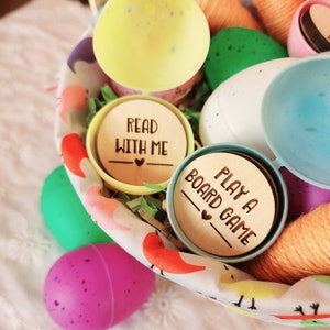 May include: A basket filled with colorful plastic Easter eggs, yarn, and wooden tokens with the text "Read with me" and "Play a board game".
