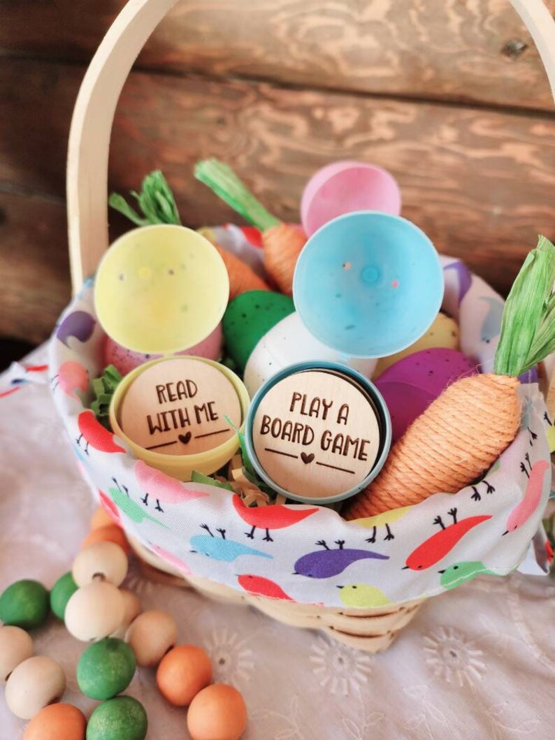 May include: A wicker basket filled with colorful plastic Easter eggs, carrots, and wooden beads. Two of the eggs have wooden lids with the text "Read with me" and "Play a board game".