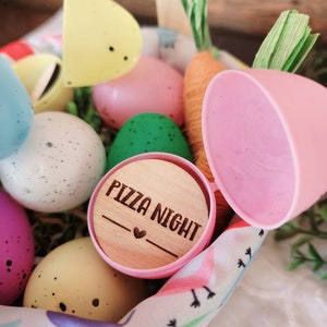 May include: A pink plastic Easter egg with a wooden lid that says "Pizza Night" with a heart. The egg is in a basket with other Easter eggs, some of which are decorated with polka dots.