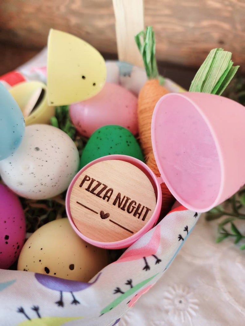 May include: A pink plastic Easter egg with a wooden lid that says "Pizza Night" with a heart. The egg is in a basket with other Easter eggs, some of which are decorated with polka dots.