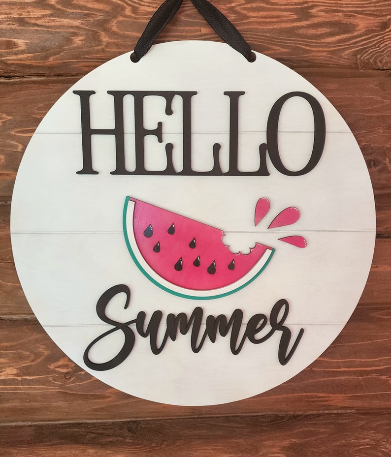 Op de afbeelding: Rond wit houten bord met de tekst "Hello Summer" in zwarte letters. In het midden van het bord staat een rode watermeloen met een hap eruit.