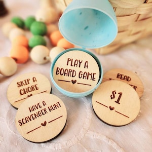 May include: Wooden tokens with different activities written on them, including "Play a Board Game", "Skip a Chore", "Have a Scavenger Hunt", and "Read a Book". The tokens are in a blue plastic egg.