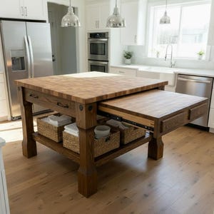 Puede incluir: Isla de cocina de madera con encimera de bloque de carnicero y extensión extraíble. La isla tiene un estante inferior con cestas tejidas y está situada en una cocina luminosa y moderna con armarios blancos y electrodomésticos de acero inoxidable.