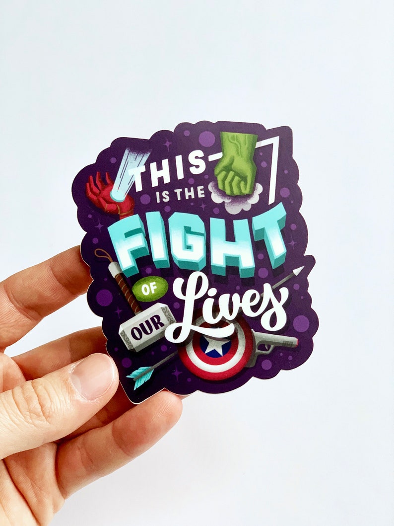 May include: Purple sticker with the text "This is the fight of our lives" in white lettering. The sticker features various superhero-themed illustrations, including a fist, a hammer, an arrow, a shield, and a gun.