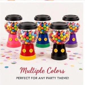 May include: Five gumball machine containers in various colours, including red, pink, blue, green, and purple, each with a black lid. The containers are filled with assorted gumballs. Text reads "Multiple Colors".