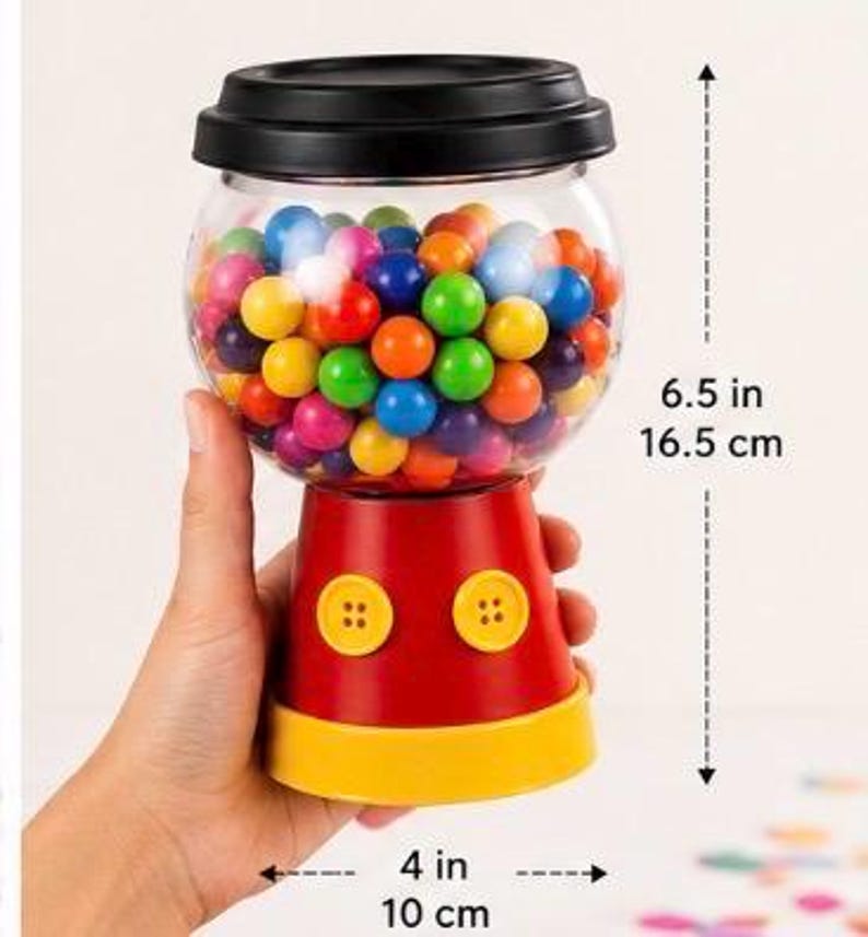 May include: A red and yellow gumball machine with a clear, round globe filled with colourful gumballs. The machine is 16.5 cm tall and 10 cm wide. It has two yellow buttons and a black lid.