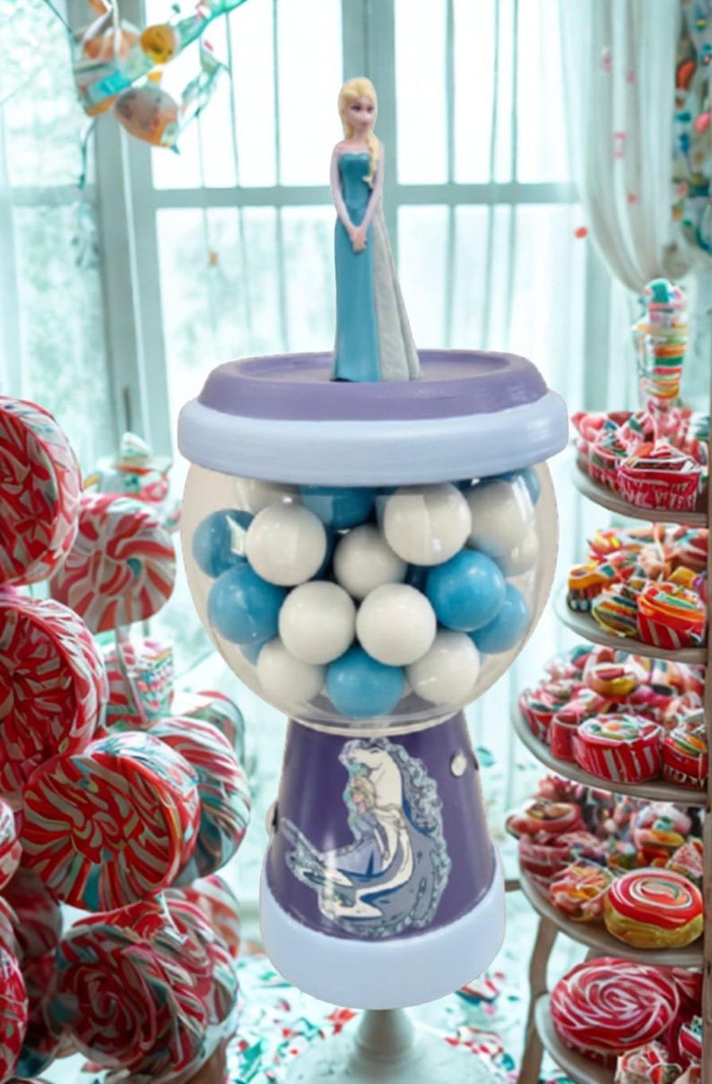 May include: A gumball machine with a purple base featuring a cartoon image of a princess. The clear globe is filled with white and blue gumballs. A figurine of the princess stands on top. The background includes colorful sweets.