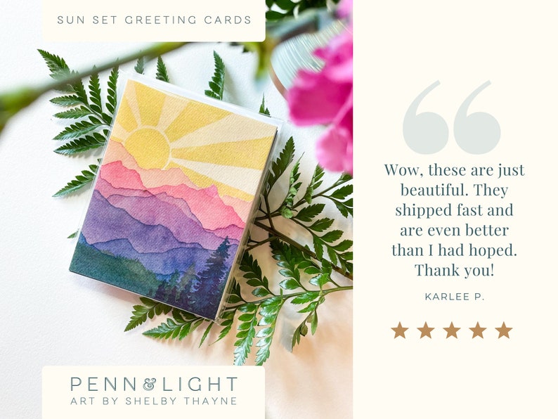 May include: A square greeting card featuring a watercolour-style illustration of a sunset over layered mountain ranges in shades of yellow, pink, purple, and blue, with dark green pine trees in the foreground. The text reads SUN SET GREETING CARDS.