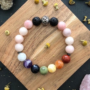 May include: A rainbow chakra bracelet with a silver charm and lava beads. The bracelet is made with rose quartz, amethyst, clear quartz, black obsidian, green aventurine, yellow jasper, carnelian, and red jasper beads.