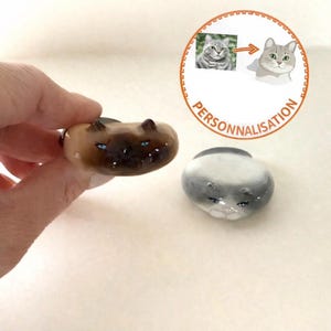 Può includere: Due statuette a forma di gatto in ceramica. Una è marrone con occhi blu, l'altra è grigia e bianca. Le statuette sono accanto a una grafica circolare con la scritta "PERSONNALISATION" e un'illustrazione di gatto.