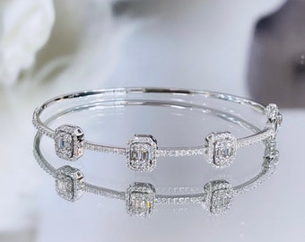 May include: A silver bangle bracelet featuring three square-shaped diamond accents. Each diamond is set in a square frame with smaller diamonds surrounding it.