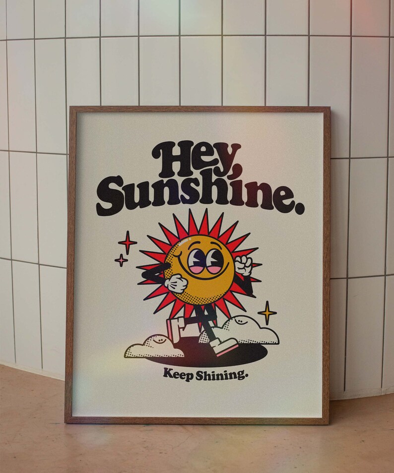 May include: A framed print with a cartoon sun character with the text "Hey, Sunshine. Keep Shining." in black and white lettering on a white background.