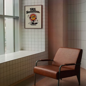 May include: A brown leather armchair with metal legs sits in a room with white tiled walls. A framed poster with the text "Hey Sunshine. Keep Shining." hangs on the wall.