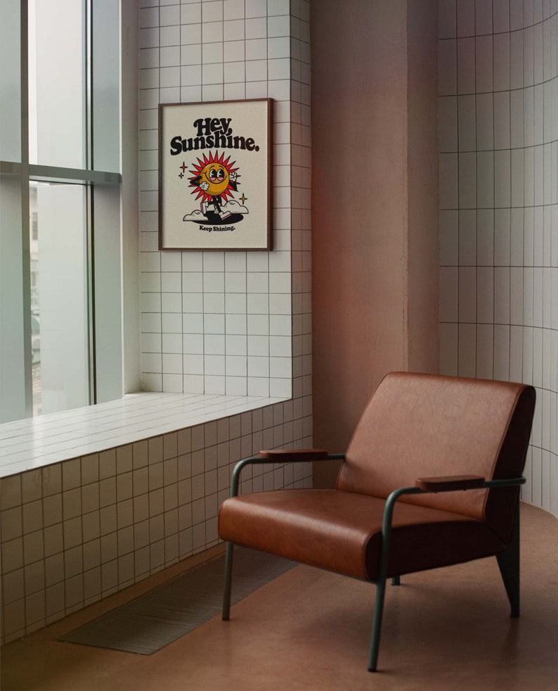 May include: A brown leather armchair with metal legs sits in a room with white tiled walls. A framed poster with the text "Hey Sunshine. Keep Shining." hangs on the wall.