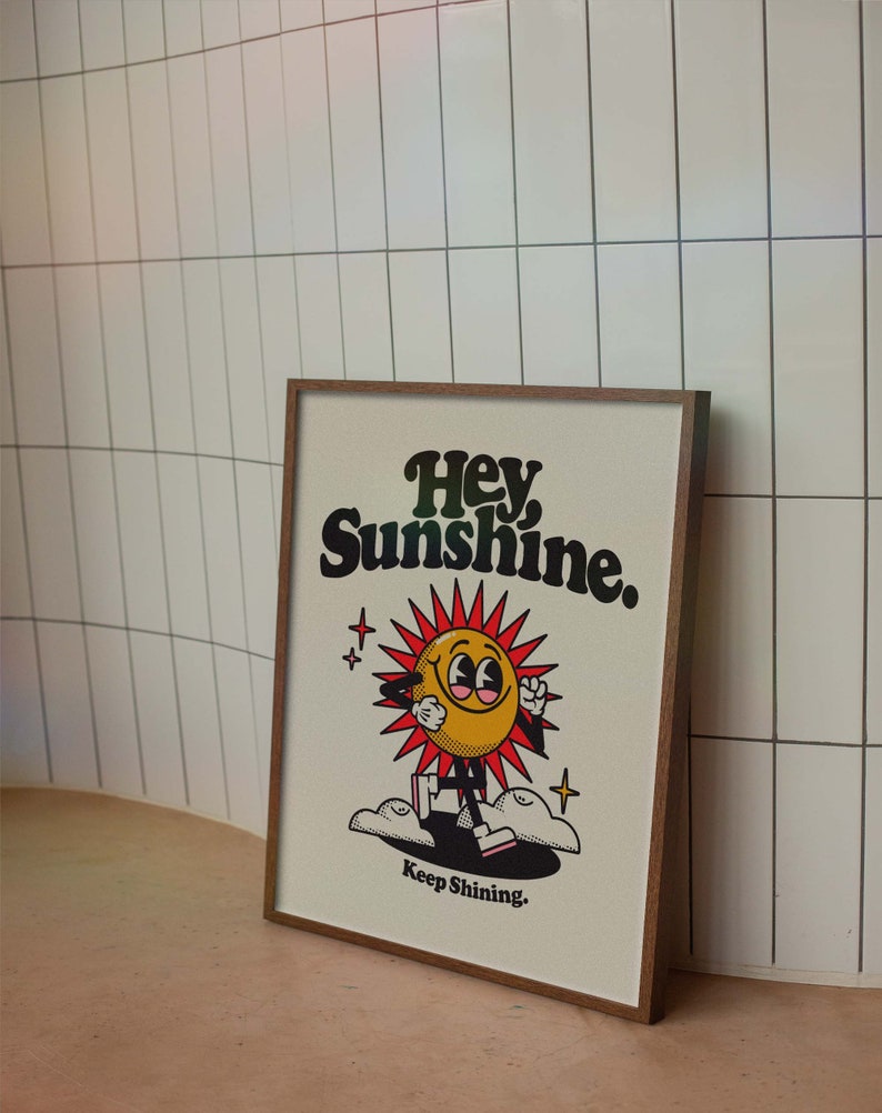 May include: A framed print with a yellow cartoon sun with a smiling face and red rays. The sun is walking on clouds and the text "Hey Sunshine. Keep Shining." is below the sun.