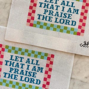 May include: Two square needlepoint canvases featuring the text LET ALL THAT I AM PRAISE THE LORD in dark blue block letters. The text is framed by a checkered border in alternating shades of pink, light blue, and lime green on white mesh.