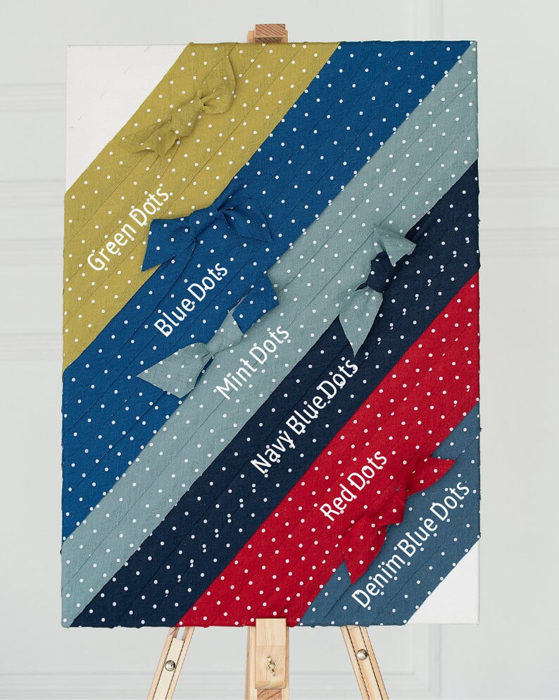May include: A wooden easel displaying fabric swatches with white polka dots in various colours, including green, blue, mint, navy blue, red, and denim blue. Each swatch has a label with the colour name and the words "Dots" written in white.