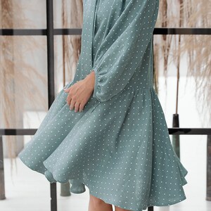 May include: A teal blue dress with white polka dots and a tie at the neck. The dress has long sleeves and a flared skirt.