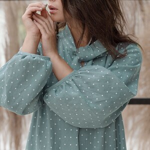 May include: A woman wearing a light blue dress with white polka dots. The dress has a gathered neckline and long sleeves.