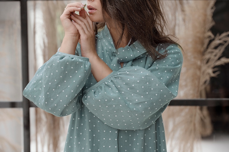 May include: A woman wearing a light blue dress with white polka dots. The dress has a gathered neckline and long sleeves.