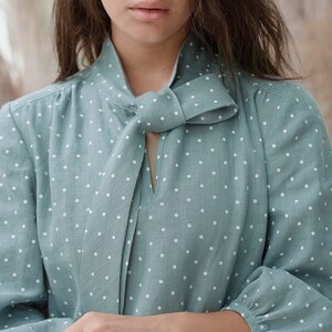 May include: A light blue blouse with white polka dots and a bow tie at the neckline.