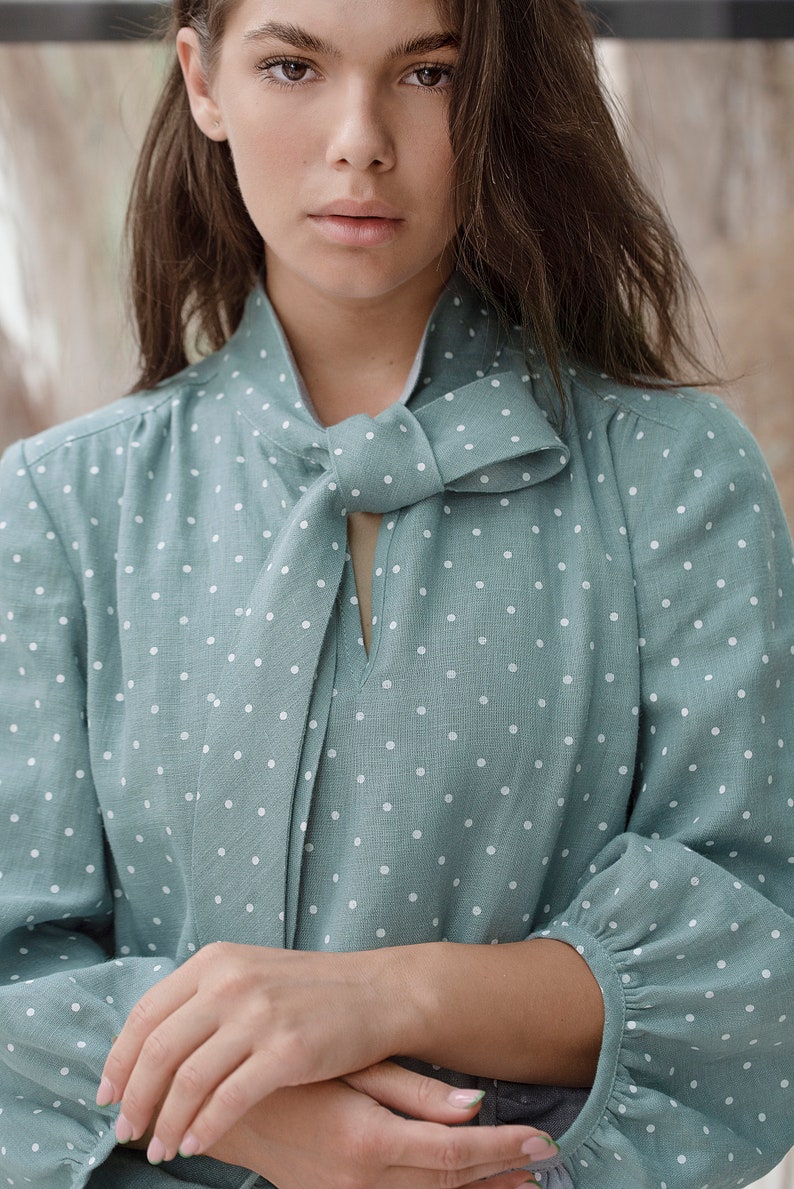 May include: A light blue blouse with white polka dots and a bow tie at the neckline.