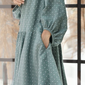 May include: A teal blue dress with white polka dots and a gathered skirt. The dress has long sleeves with a gathered cuff and a pocket on the left side.