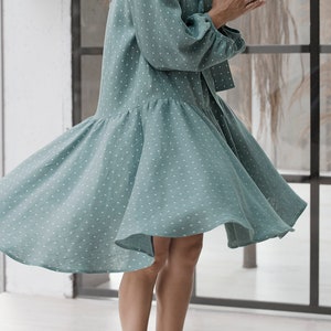 May include: A light blue dress with white polka dots. The dress has a ruffled hem and a long sleeve. The dress is made of a lightweight fabric and is perfect for a summer day.