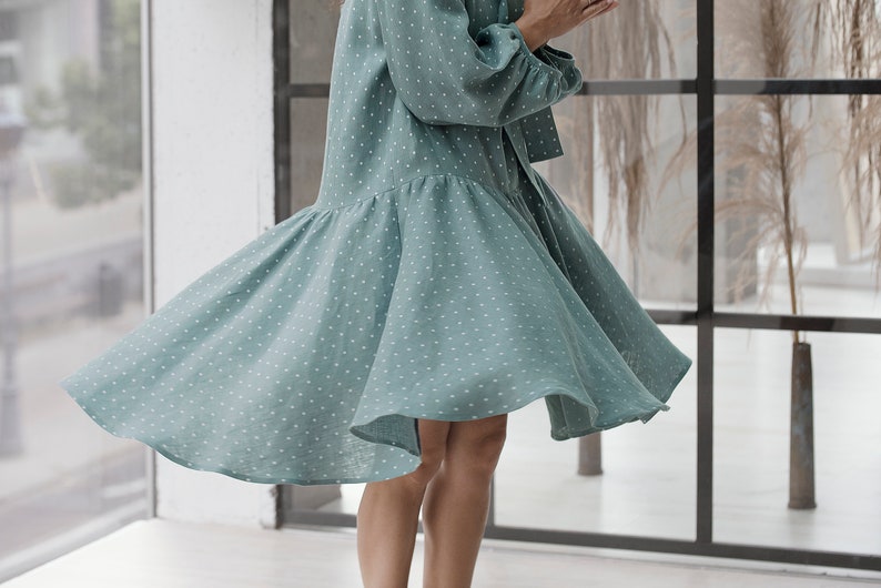 May include: A light blue dress with white polka dots. The dress has a ruffled hem and a long sleeve. The dress is made of a lightweight fabric and is perfect for a summer day.