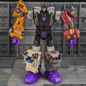 May include: A large, articulated robot toy with a black torso, gray and purple accents, and limbs that transform into vehicles. The toy has yellow, red, and beige vehicle components, and purple hands and feet. The robot stands on a gray surface.