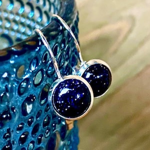 May include: A pair of silver dangle earrings with dark blue round stones. The stones have a sparkly, speckled texture.