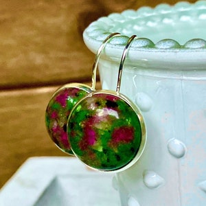 May include: A pair of silver dangle earrings with round green and pink gemstone cabochons.