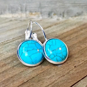 May include: A pair of silver hoop earrings with turquoise blue cabochon stones. The stones have a marbled pattern.