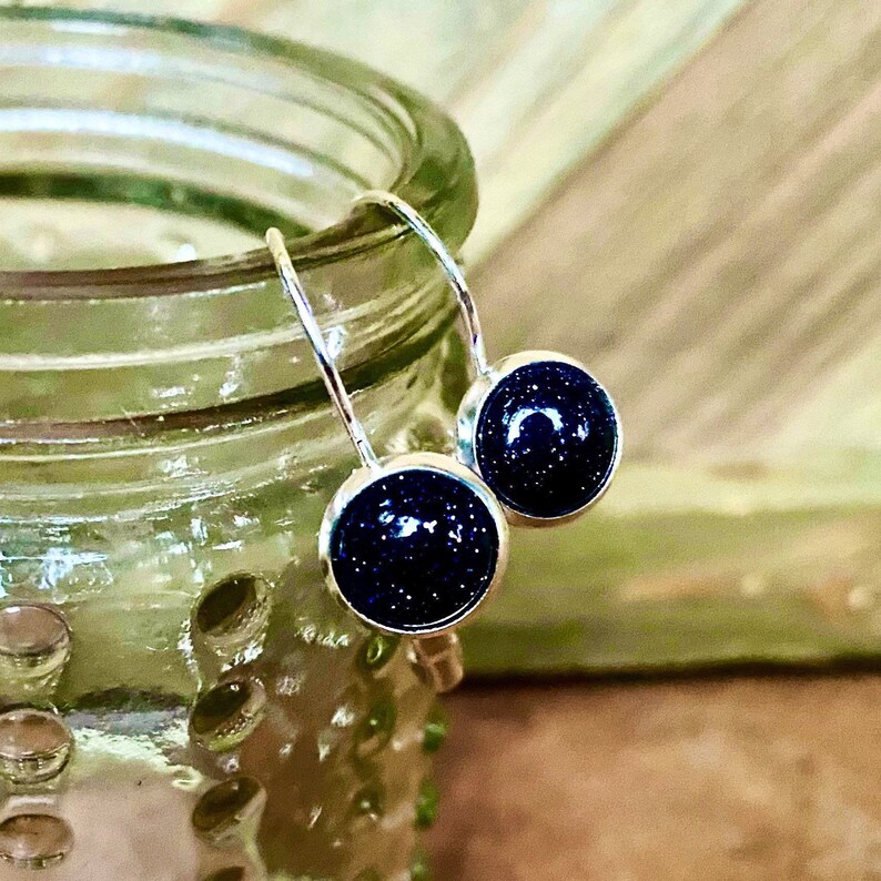 May include: A pair of silver dangle earrings with dark blue round stones. The stones have a speckled texture.