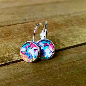 May include: A pair of round leverback earrings with a colorful abstract design. The earrings feature a silver-tone metal setting and a vibrant pattern of pink, blue, and orange hues on a white background.