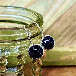 May include: A pair of silver dangle earrings with small round blue gemstone accents. The gemstones have a sparkly, speckled texture.