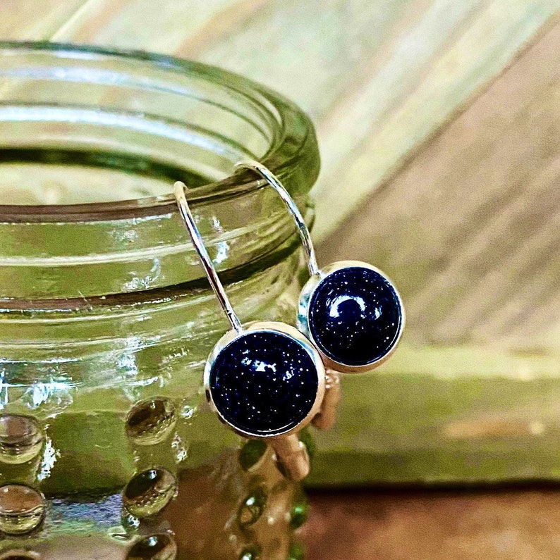 May include: A pair of silver dangle earrings with small round blue gemstone accents. The gemstones have a sparkly, speckled texture.