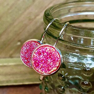 Può includere: Un paio di orecchini pendenti in argento con pietre rotonde a cabochon con glitter rosa.