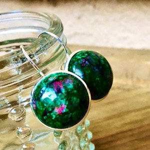 May include: A pair of round dangle earrings. Each earring has a vibrant green and pink marbled stone set in a silver-tone bezel. The earrings are suspended from silver-tone ear wires, showcasing a natural, artistic design.