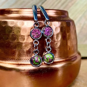 Könnte beinhalten: Ein Paar Hängeohrringe mit zwei runden, glitzernden, rosa und grünen Steinen an jedem Ohrring. Die Ohrringe sind silberfarben und haben ein Kettenglied zwischen den Steinen.