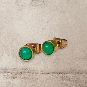 May include: A pair of gold stud earrings with green gemstone accents.